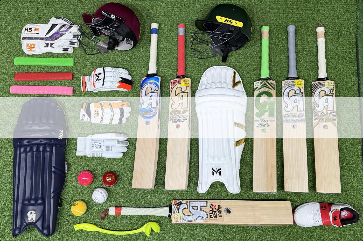 Collection of cricket equipment including bats, helmets, gloves, and pads on a green surface.